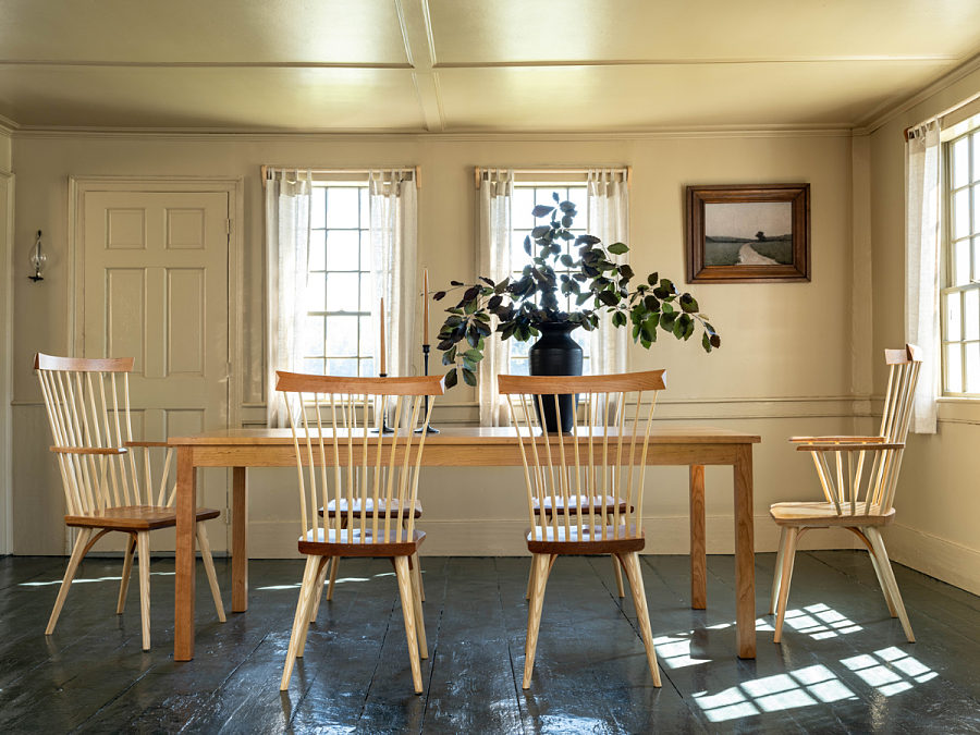 Eastward Dining Chairs and Table in cherry in a living room with green painted wood flors and a vase with grenery on the table.