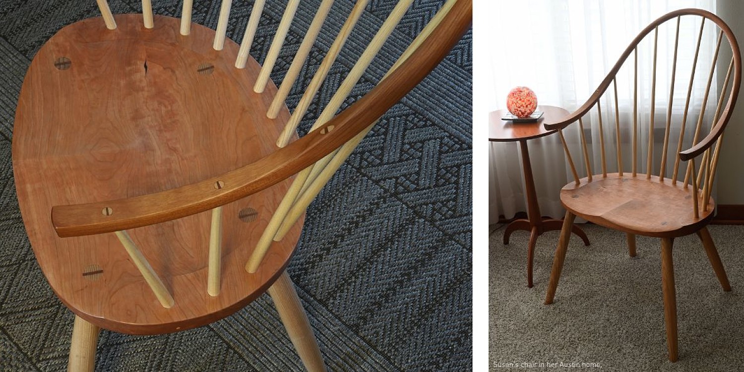 detail of a the arm on the continuous arm chair in cherry (left). To the right is the continuous arm chair in cherry set beside a shaker round stand in cherry with a orange glass paperweight on the table top. The floor has grey carpeting and there are curtains hanging behind the chair and table