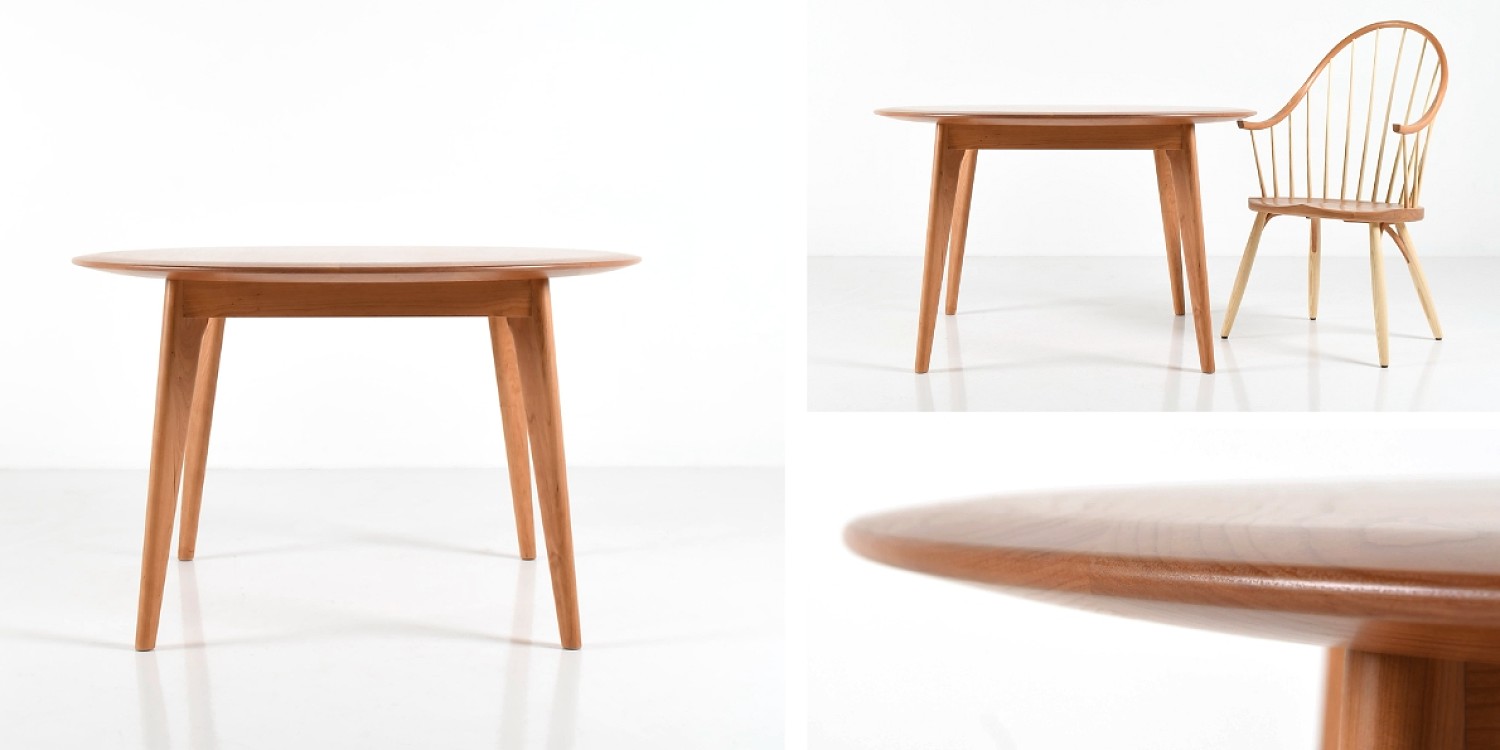 A wooden table with a round top and splayed legs in cherry. Unity Round Top table with the Continuous Arm Chair. Detail of the table top