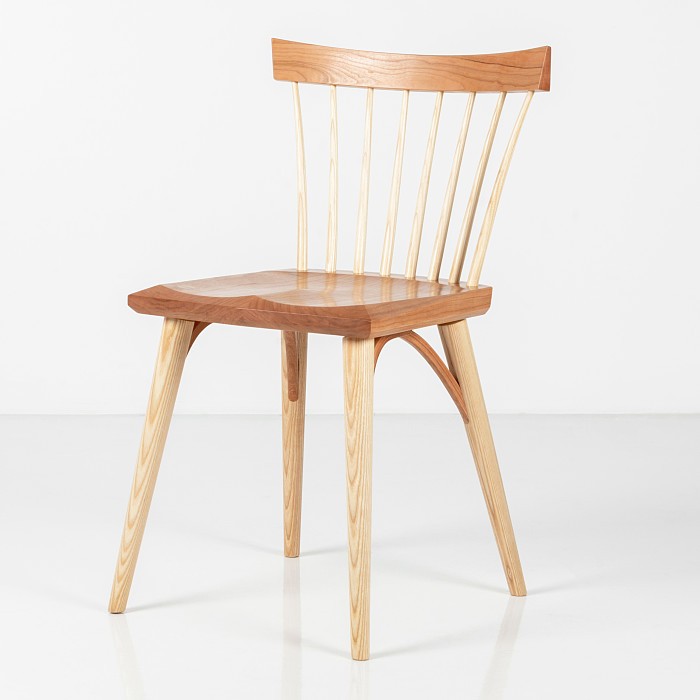 Eastward studio chair in cherry in a white studio. The chair has spindles in ash that meet a cherry seat and crest. The legs are also made of ash.
