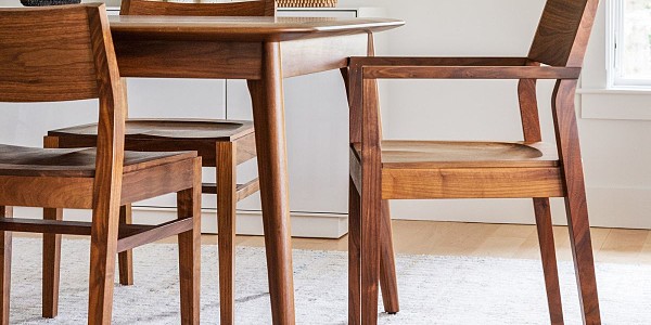 An open concept kitchen and dining room with the unity table and pacific chairs int he foreground. In the kitchen there are island stools around a live edge kitchen island. A mirror and artwork decorates the wall behind the table and chairs.