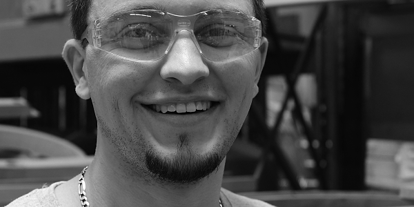 black and white image of craftsman Mason F. He is wearing clear safety goggles and a grey Thos. Moser tshirt.